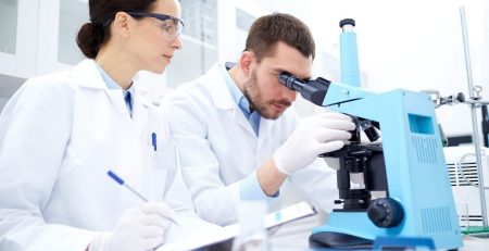 Researchers at a microscope and taking notes 