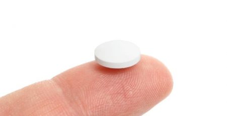Small, white round pill, sitting on a finger tip