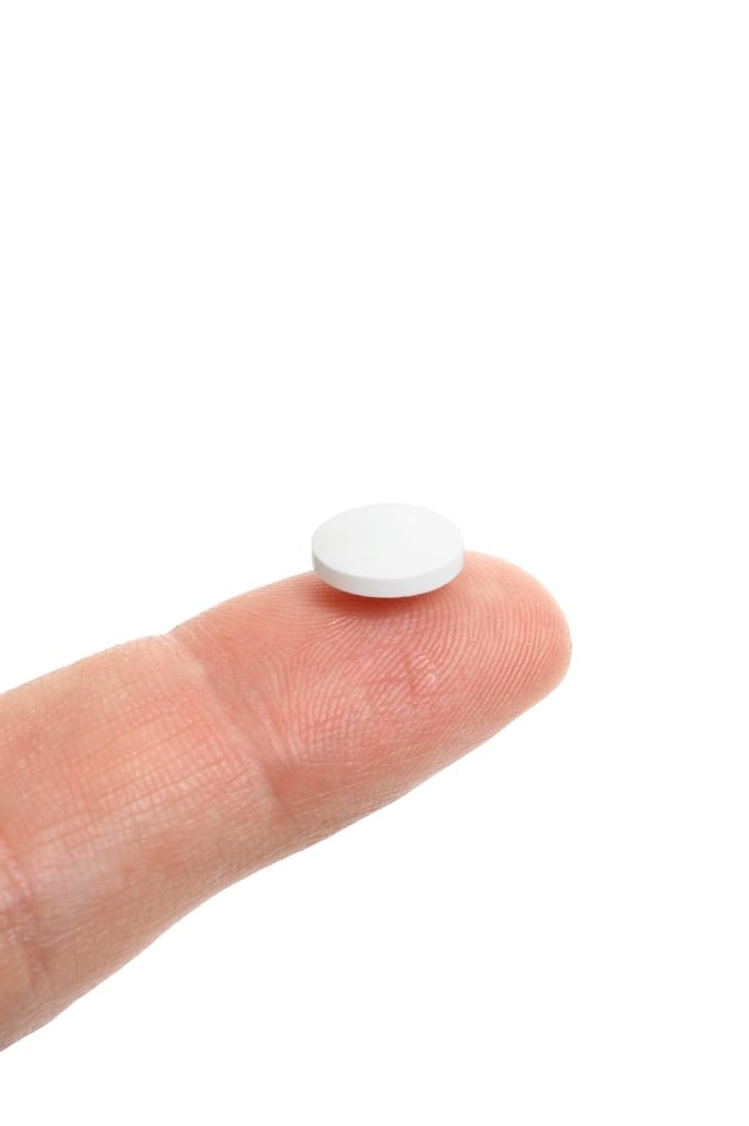 Small, white round pill, sitting on a finger tip